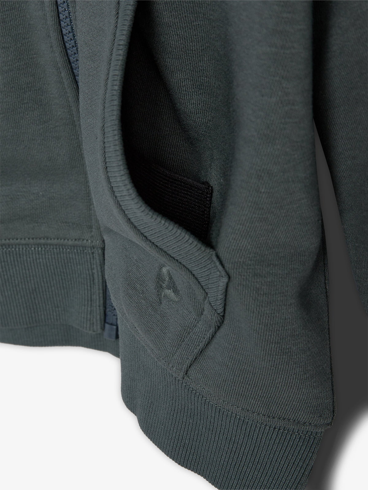 A dark-colored jacket with a visible pocket and zipper. The fabric appears ribbed, and the jacket hangs loosely, suggesting it is either worn or displayed on a hanger.