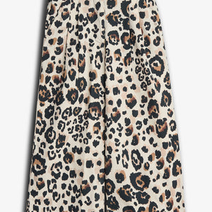 Beige knee-length shorts feature a bold leopard print pattern, including black and brown spots. They have a pleated front and button closure, set against a plain white background.