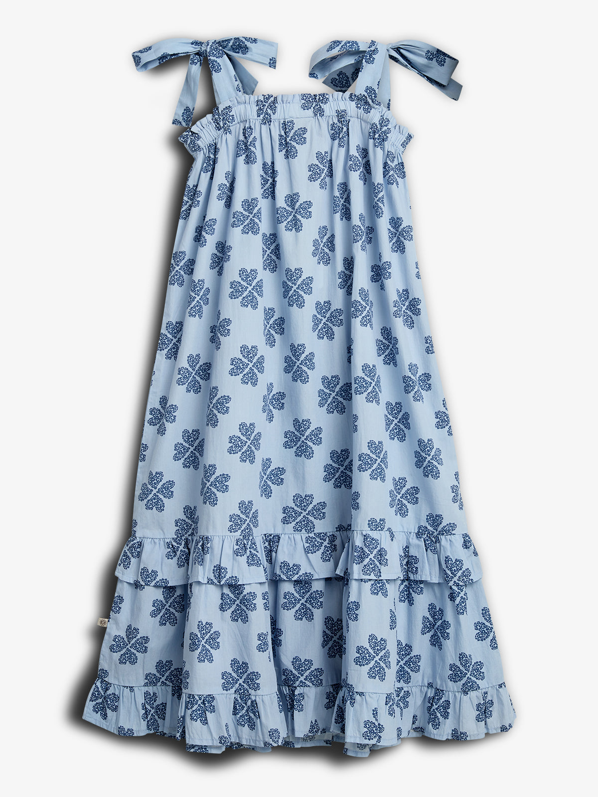 A light blue, sleeveless dress with blue floral patterns and ruffled tiers hangs against a plain background. The dress features bow-tied shoulder straps, enhancing its charming, summery design.