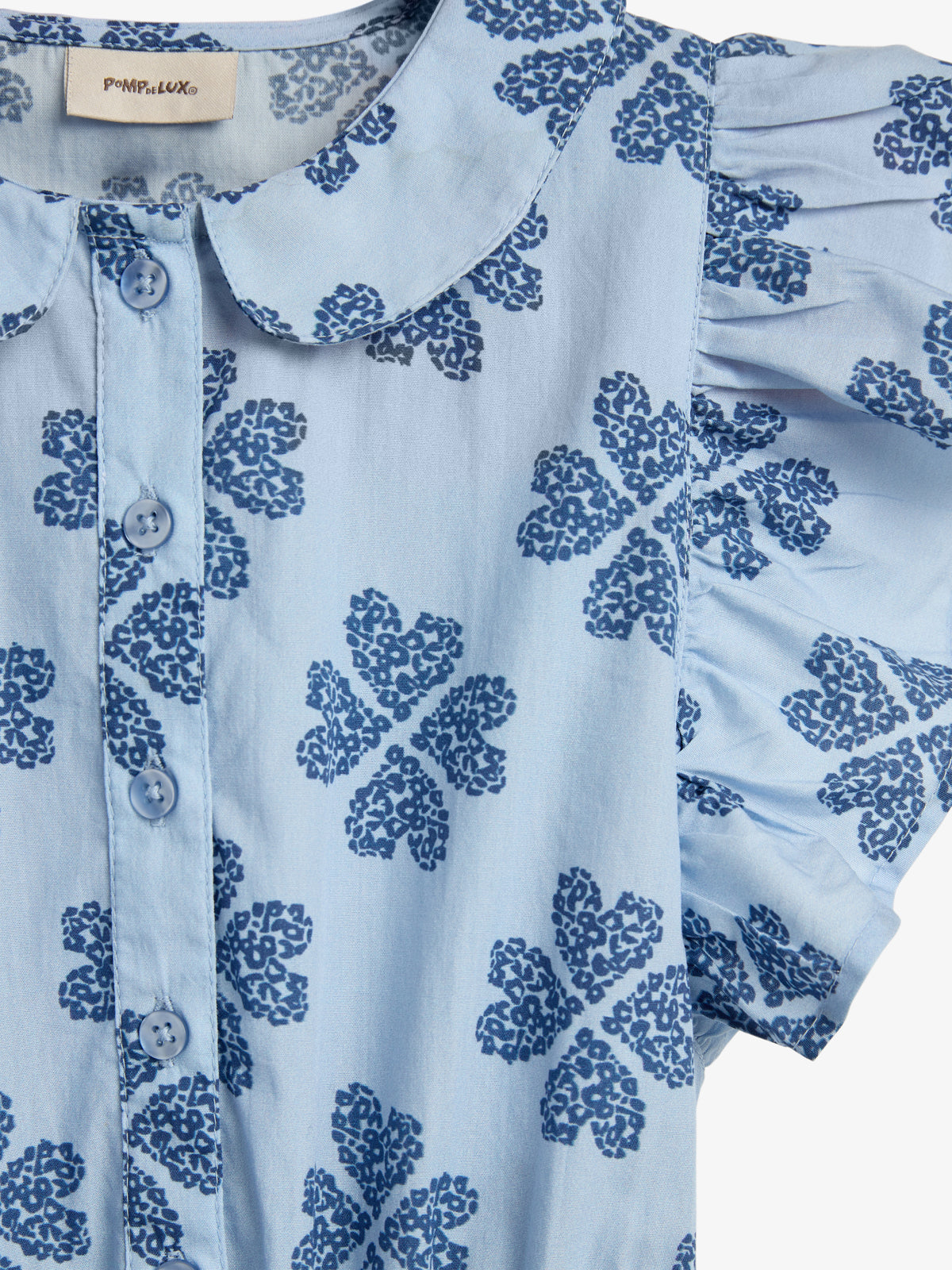 The blue shirt features a floral pattern with dark blue flowers, a Peter Pan collar, and button-down front. It is displayed against a plain background. A label reads "POMPdeLUX."