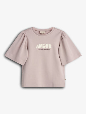 A lavender T-shirt with puffed sleeves displays "AMOUR" and "J'ADORE LE SOLEIL" printed on the front. It hangs against a plain white background.
