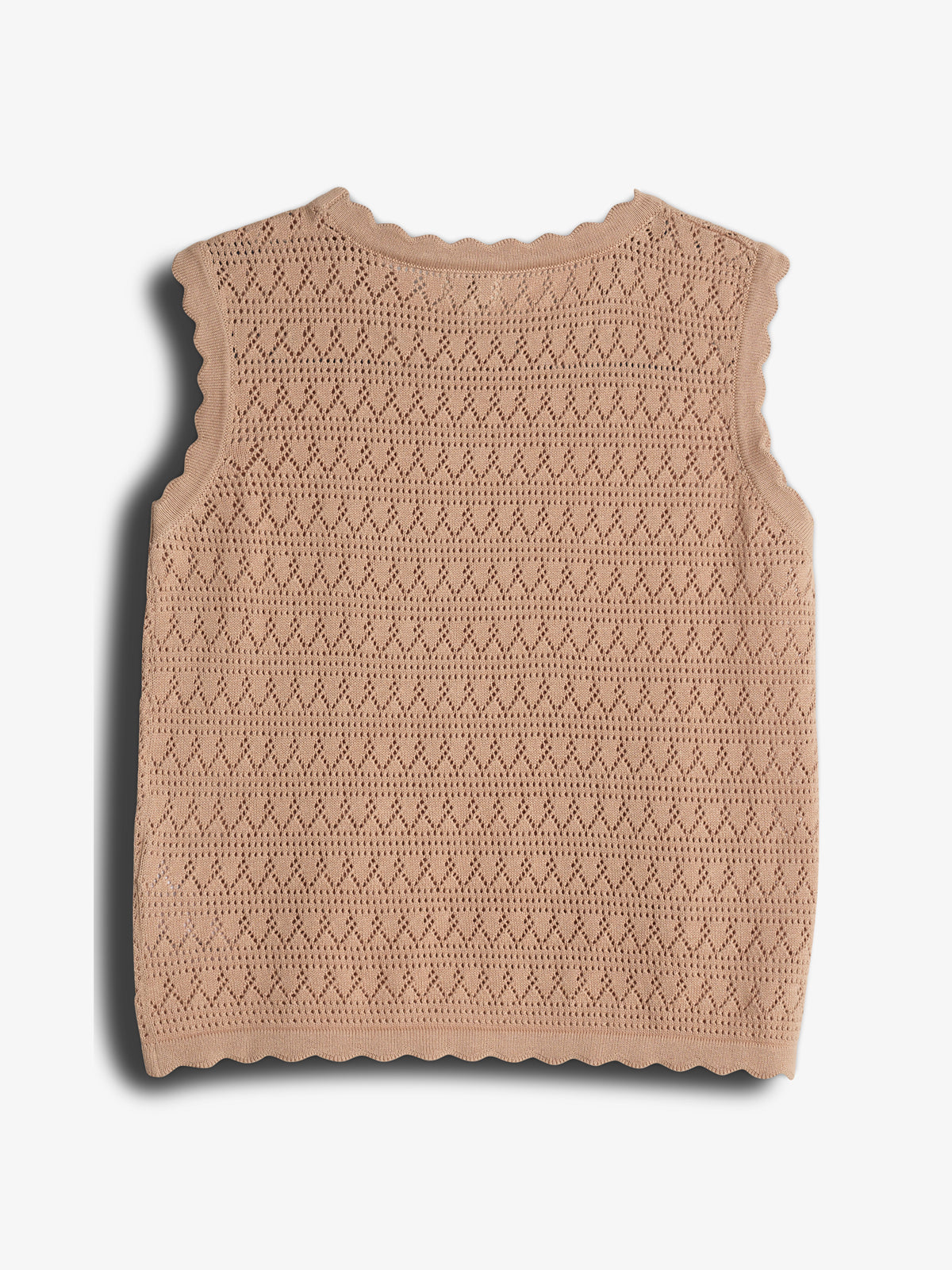 A sleeveless knitted beige top features a scalloped edge and intricate diamond patterns, resting on a plain white background, casting a soft shadow.