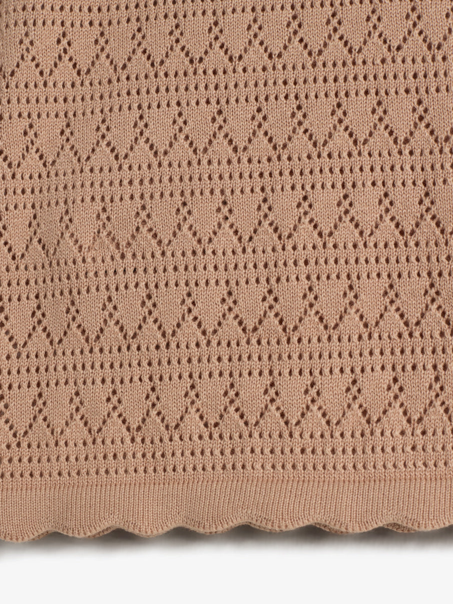 The object is a knitted fabric featuring a repeating diamond pattern with eyelets. It is beige in color, with a scalloped edge. The fabric appears flat and neatly arranged.