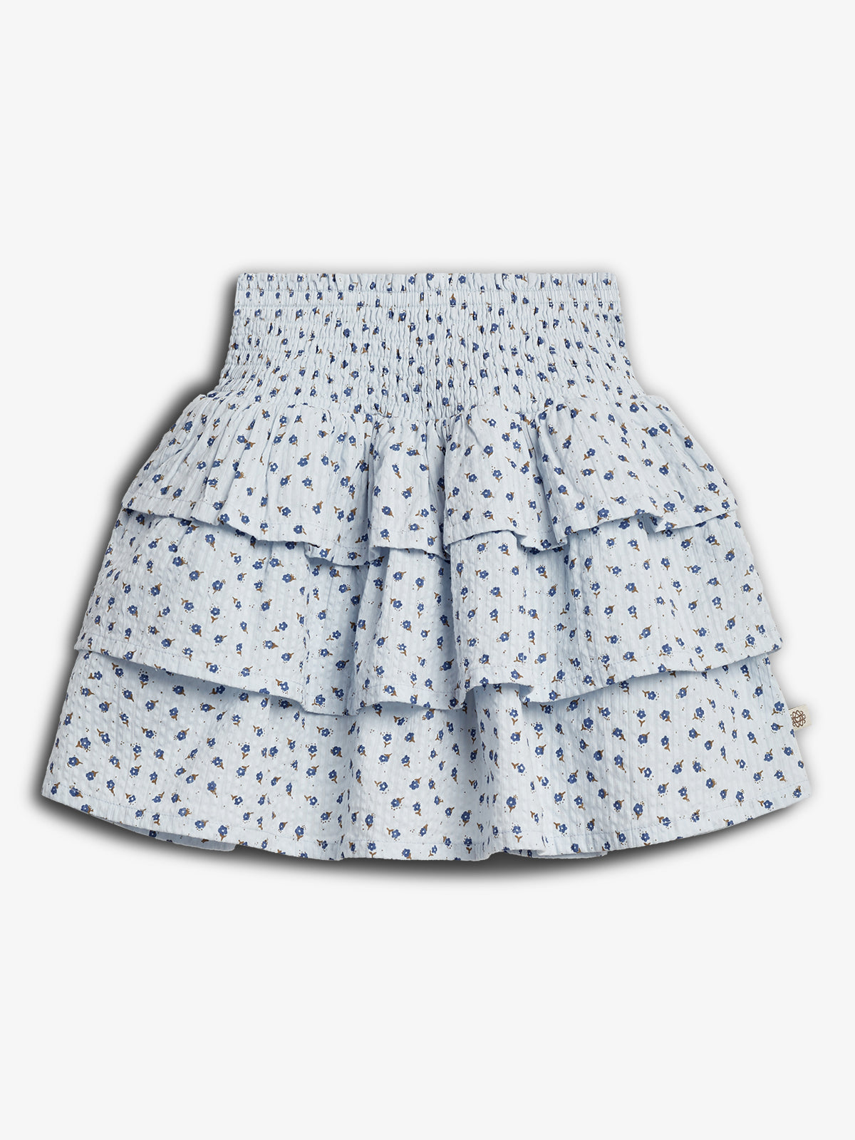 A light blue, tiered skirt with a floral pattern features small blue flowers. It has a smocked waistband and a layered, ruffled design, set against a plain white background.