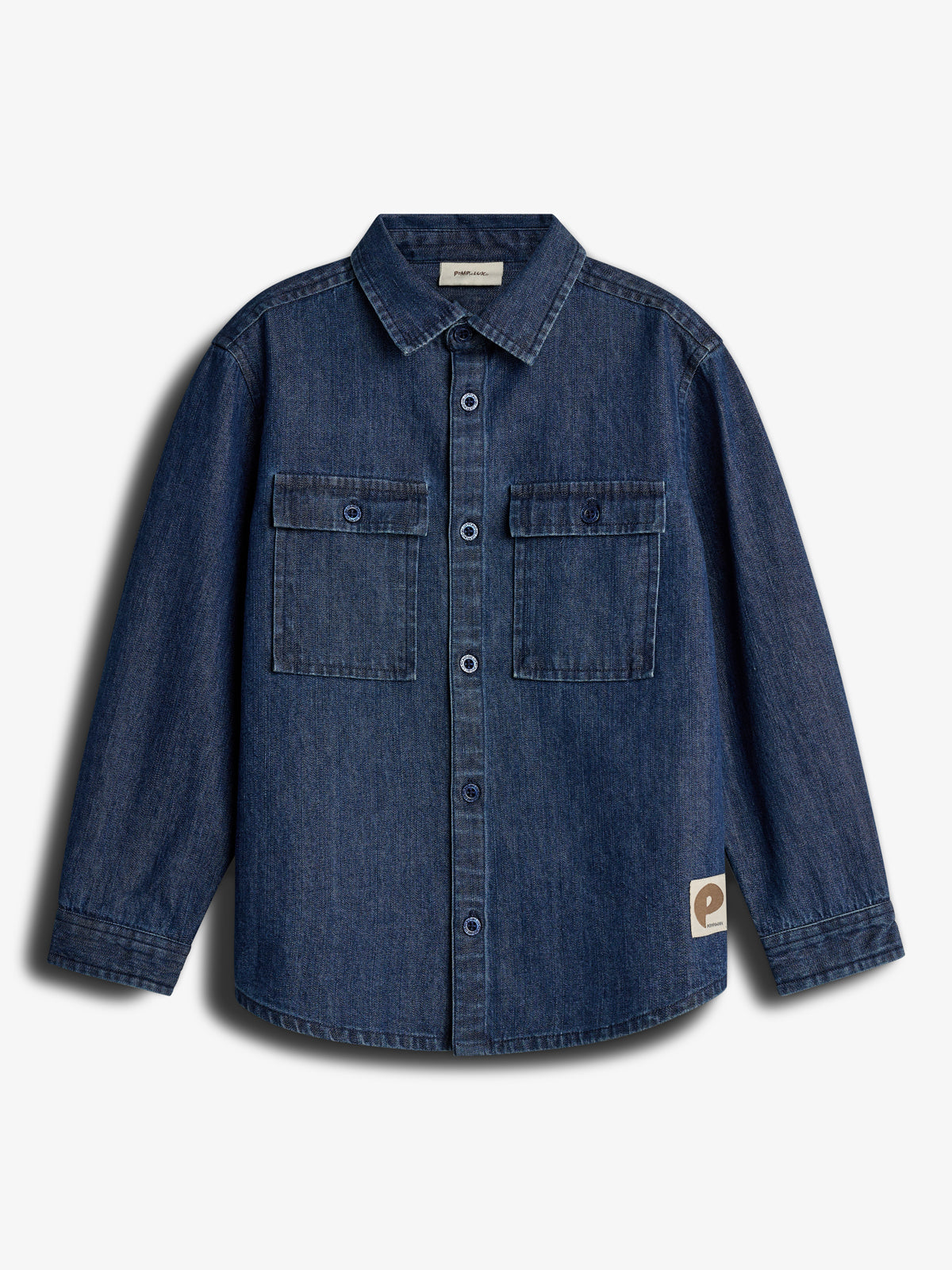 Denim shirt displayed, featuring long sleeves, buttoned front, and two chest pockets. Labels read "paperless" inside collar and logo tag on lower side. Set against a plain white background.