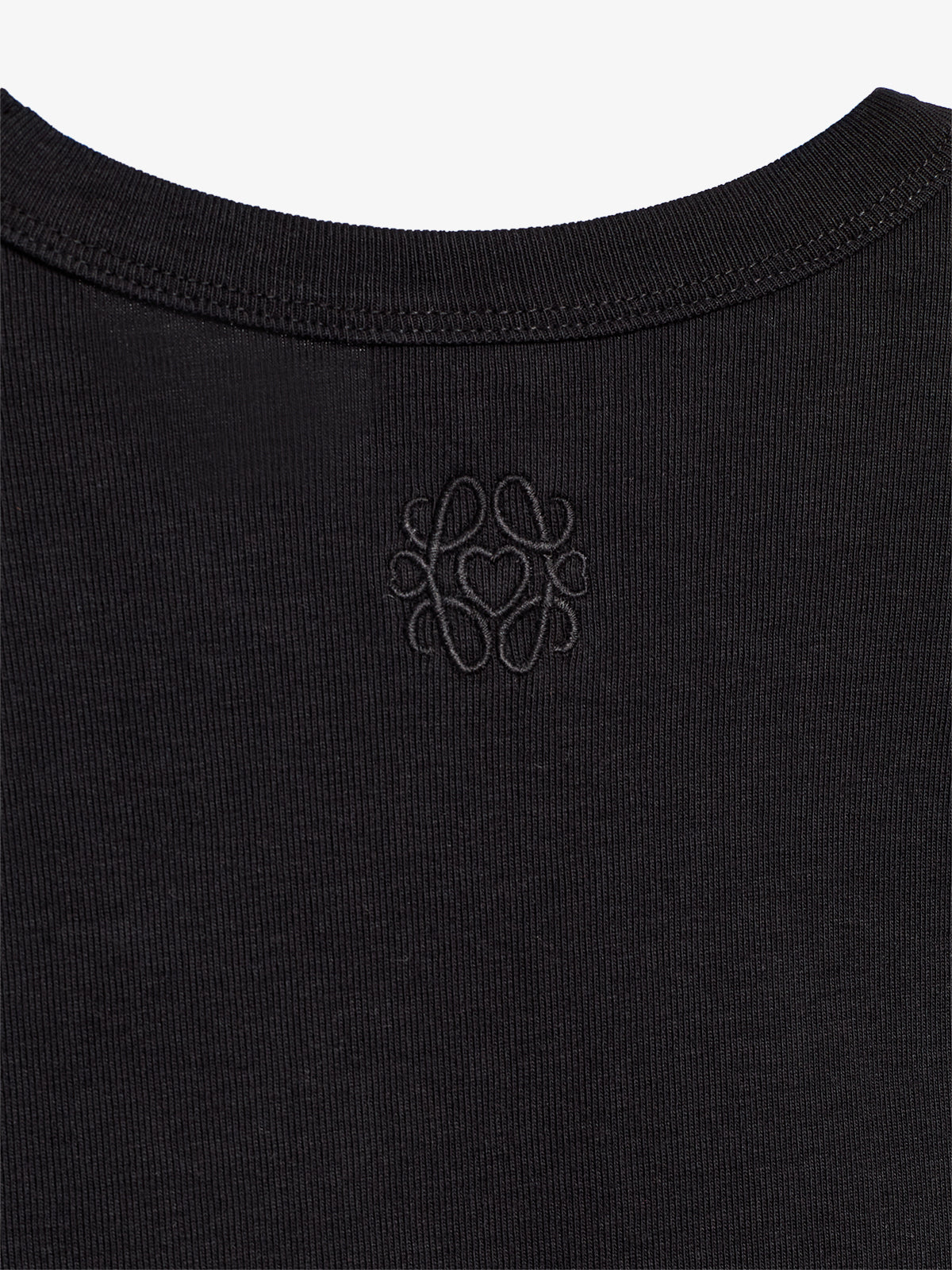 Auf einem schwarzen T-Shirt ist direkt unter dem Kragen ein stilisiertes, eingeprägtes Design mit ineinander verschlungenen Buchstaben zu sehen, umgeben von einem unifarbenen Hintergrund.