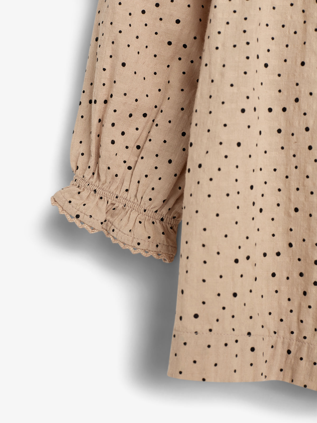 Beige fabric with black polka dots hangs loosely, featuring ruffled cuffs. The material appears lightweight, suggesting a garment for casual wear. Shadows cast to the left indicate natural lighting.