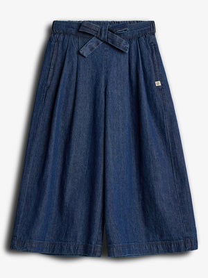 Wide-legged denim culottes feature a tied waist and deep pleats, displayed against a plain white background. A small logo tag is attached on the right side.