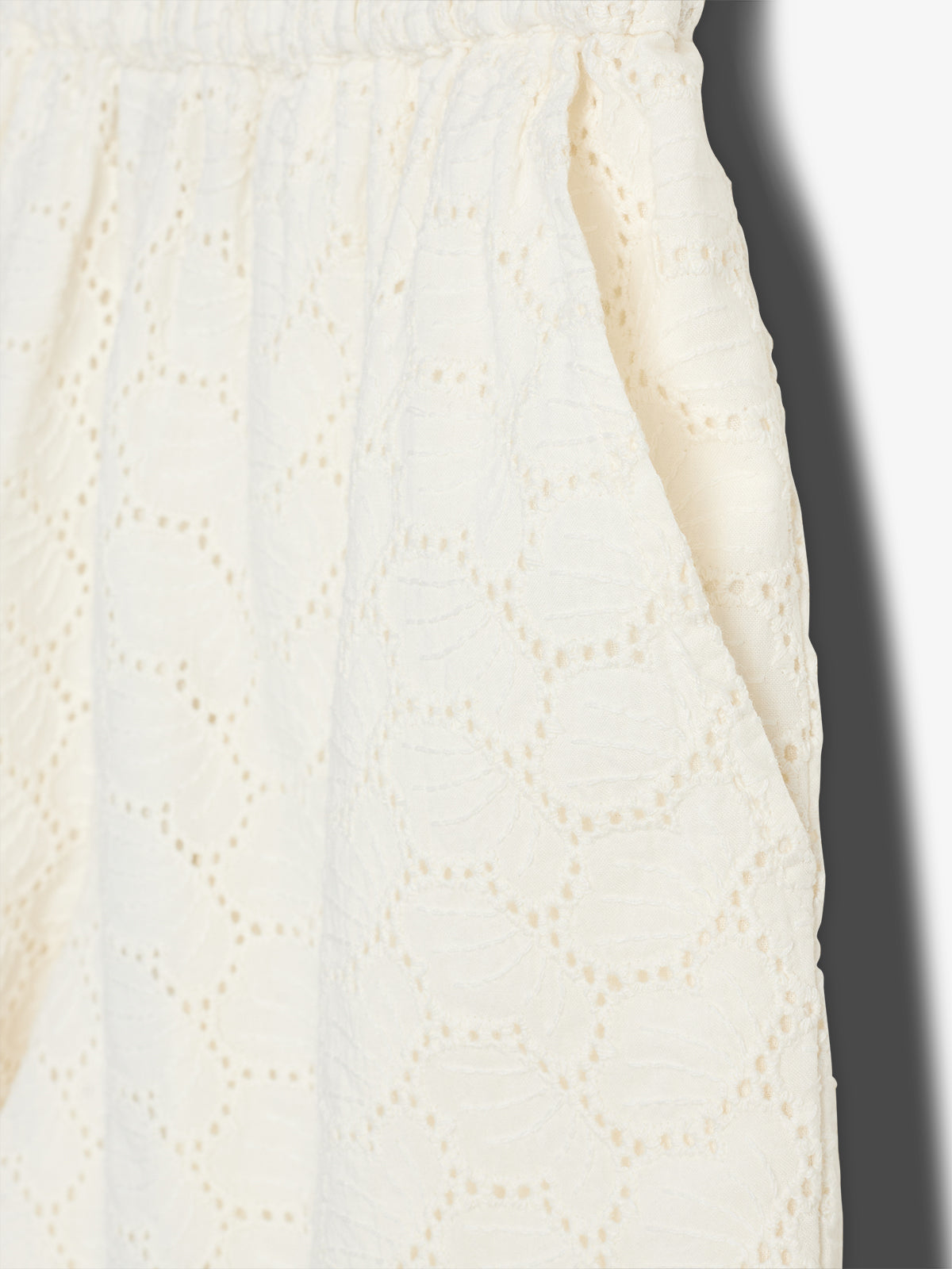 Cream, lace-textured fabric with a hexagonal pattern hangs loosely in soft folds, set against a plain background, showcasing intricate design and texture.