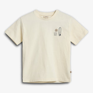 Cream-colored T-shirt displaying a minimalist design featuring a sun, waves, and a surfboard on the left chest. The background is plain white, emphasizing the shirt's simplicity.