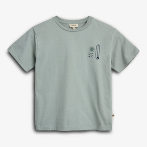 A light green short-sleeved T-shirt features a small graphic with a sun, waves, and a surfboard on the left chest area. The shirt is displayed on a plain background.