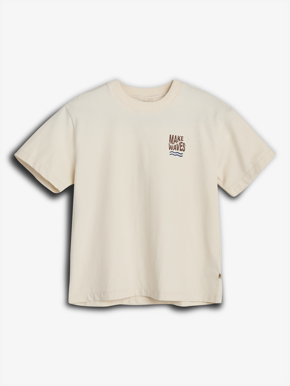 Cream-colored T-shirt features bold text "MAKE WAVES" with a wave graphic underneath, positioned on the left chest, against a plain white background.