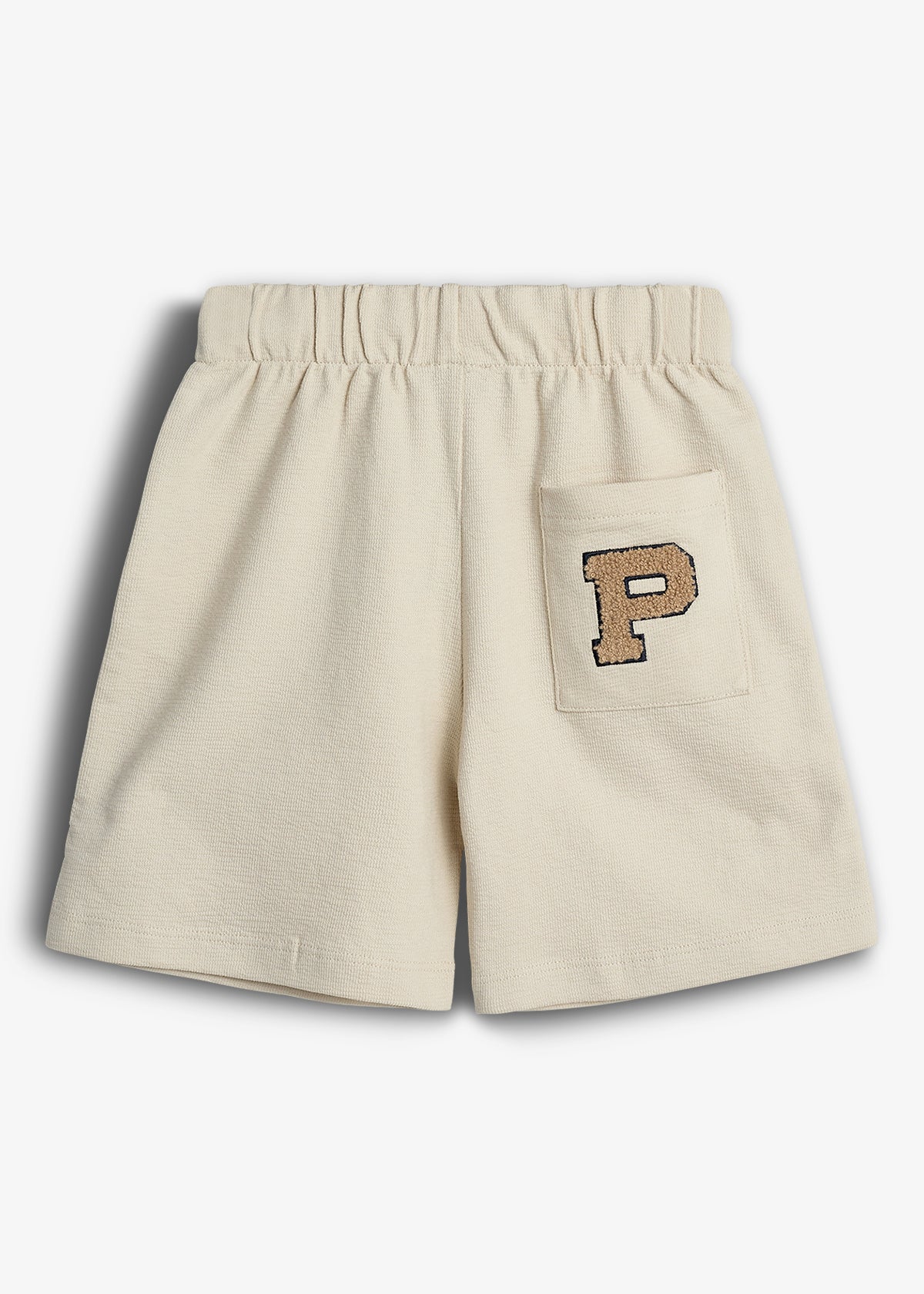 Beige shorts with an elastic waistband feature a rectangular back pocket. The letter "P" is embroidered on the pocket. The background is plain white.