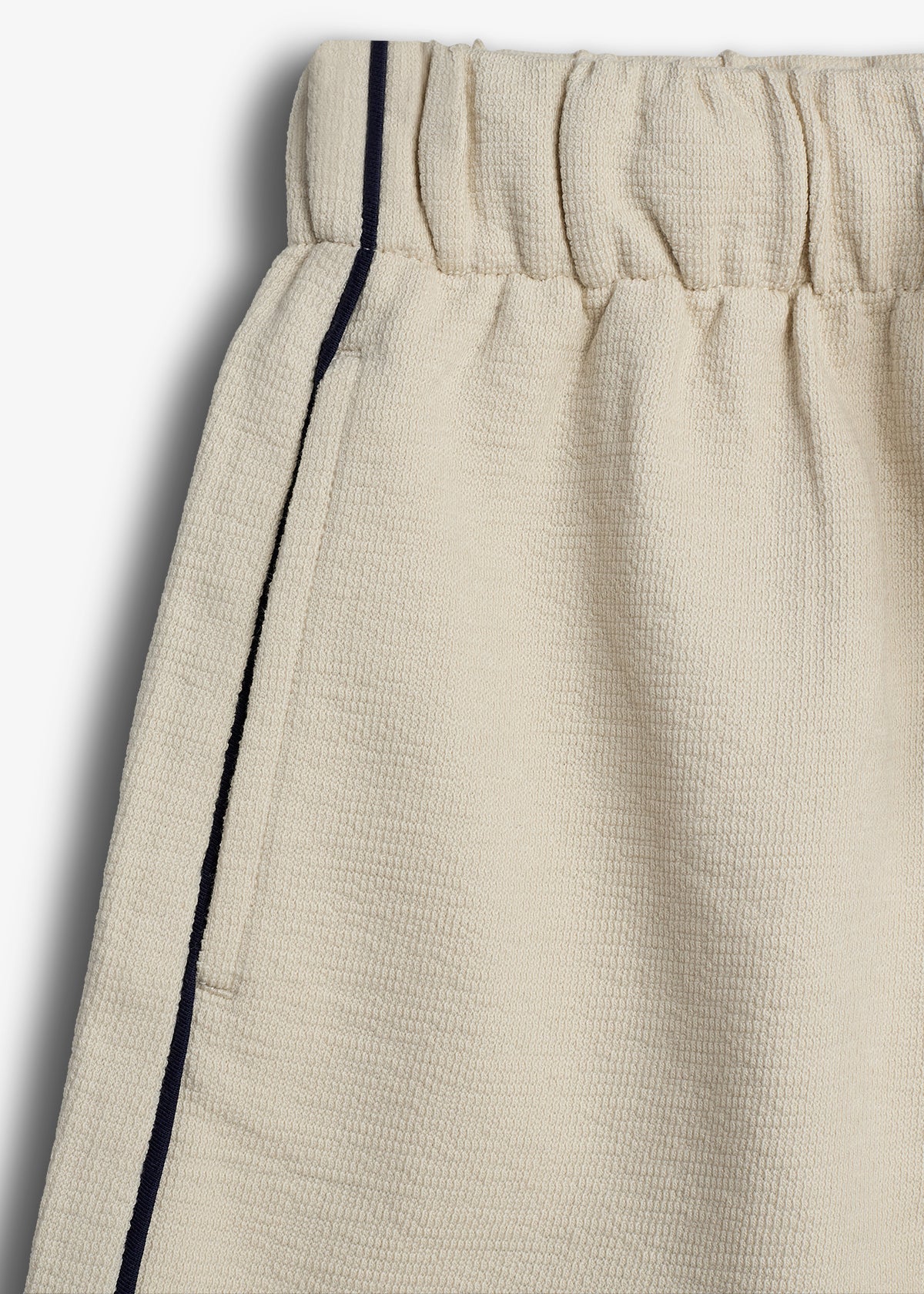 Beige fabric shorts with an elastic waistband and a black vertical stripe along the seam, against a plain white background.