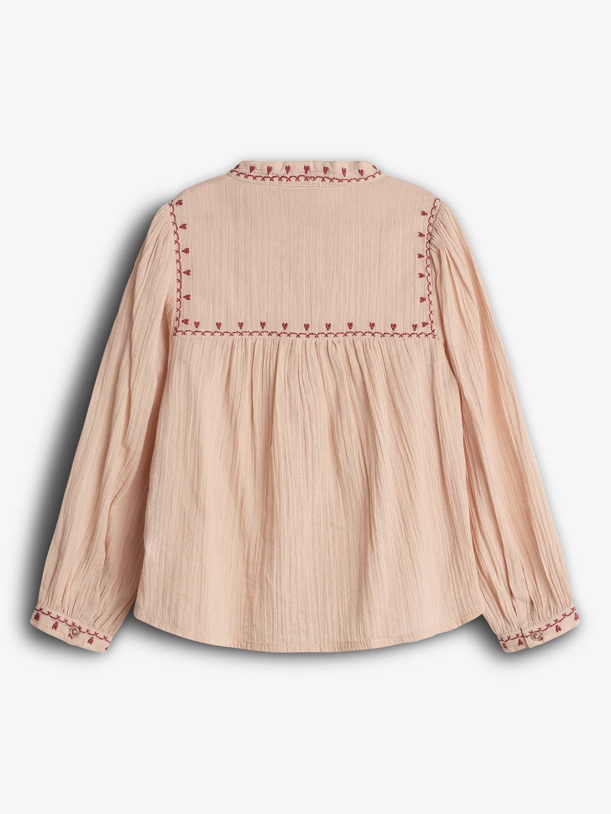 A peach-colored blouse with red embroidered patterns along the back yoke and cuffs, displayed against a plain background. The fabric appears crinkled, and the sleeves are long and gathered.