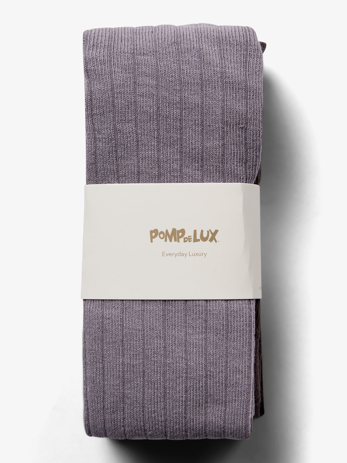 Ein gerolltes, lila gestricktes Kleidungsstück liegt in einer weißen Banderole mit der Aufschrift "POMPdeLUX Everyday Luxury" auf einer weißen Oberfläche.
