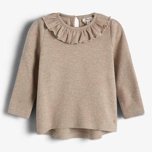 Ein beige Pullover mit langen Ärmeln und Rüschendetail am Hals hängt vor einem weißen Hintergrund. Ein kleines Metallemblem befindet sich am unteren Rand.
