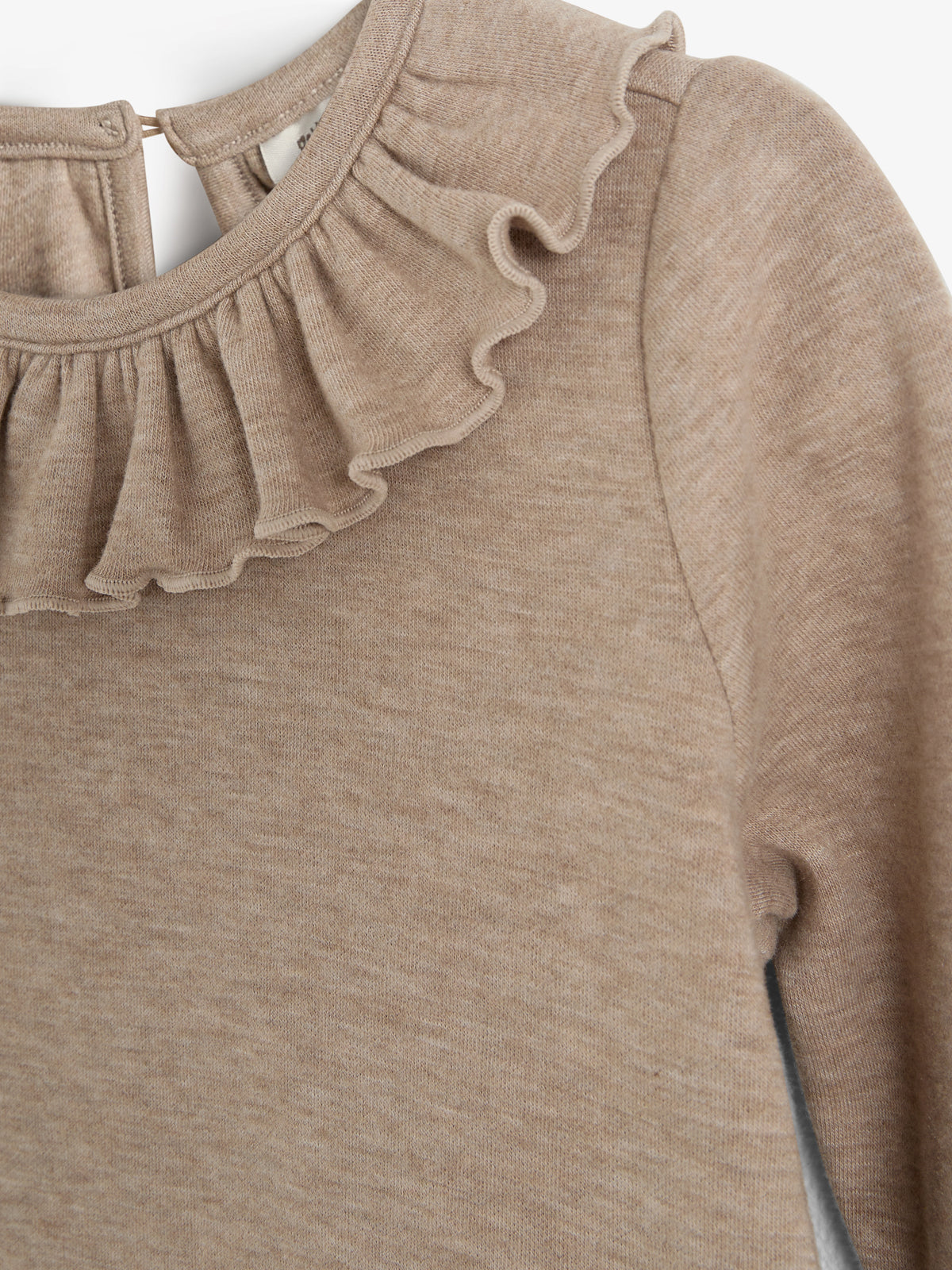 Ein beige Pullover mit langen Ärmeln zeigt eine gerüschte Halskrause. Der Hintergrund ist neutral, wodurch der Fokus auf das sanfte Textilmuster und die Details des Kleidungsstücks liegt.