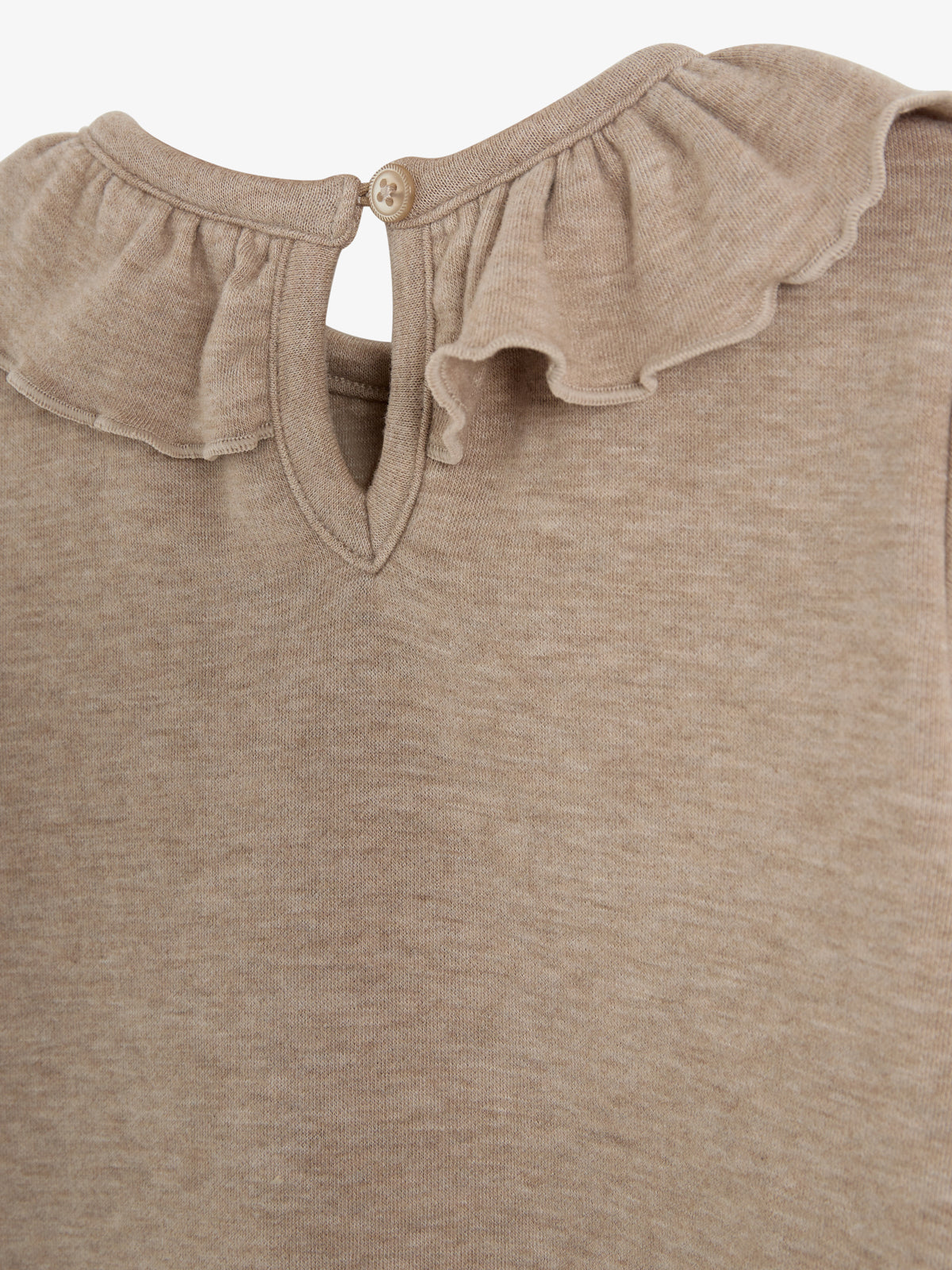 Ein beige Oberteil mit Rüschen am Hals besitzt eine Knopföffnung. Der Stoff wirkt weich und gleichmäßig strukturiert.
