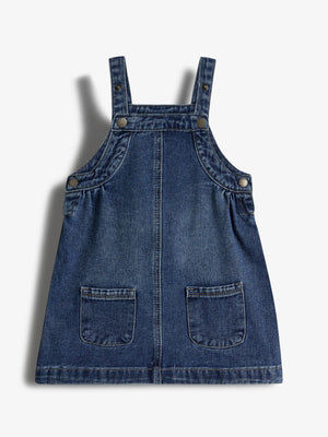 Jeanskleid mit Trägern, verziert mit Knöpfen und zwei aufgesetzten Taschen vorne. Liegt auf einem weißen Hintergrund.