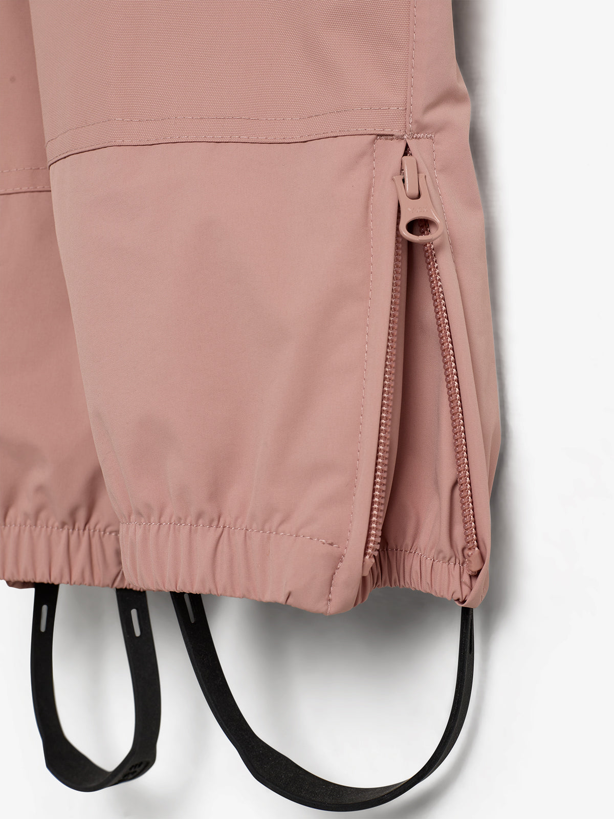 Rosa Stoffhose mit seitlichem Reißverschluss und elastischem Band, hängt in einem neutralen, hellen Raum. Zwei schwarze Bänder ragen am unteren Ende heraus.