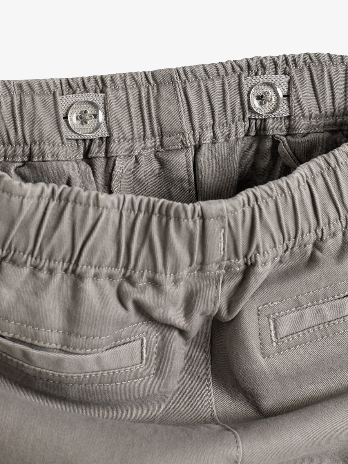 Graue Hose mit elastischem Bund und zwei Knöpfen. Die Rückseite zeigt zwei angedeutete Taschen. Umgebung ist neutral ohne erkennbare Muster oder zusätzliche Elemente.