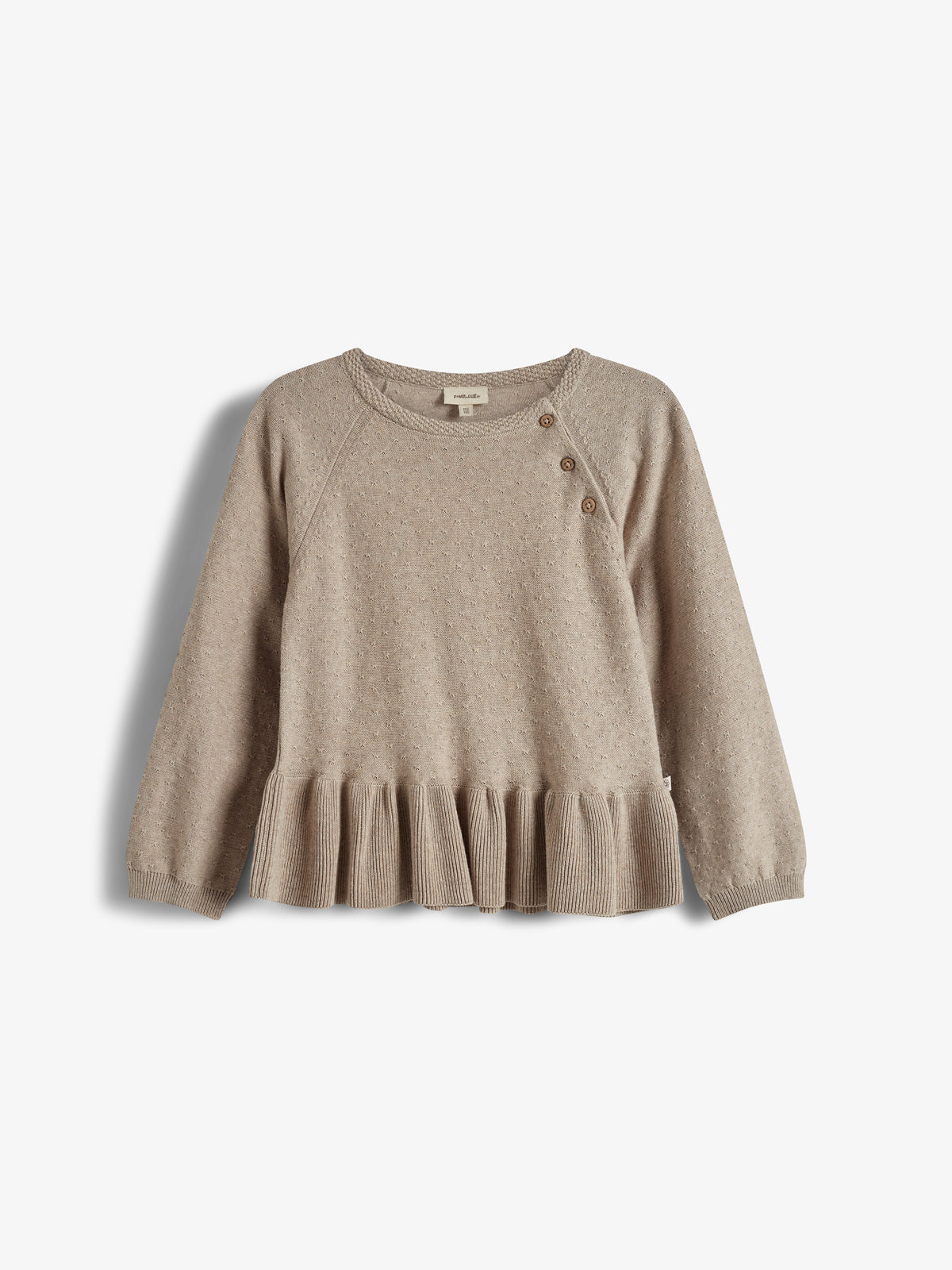 Ein beiger Pullover mit langen Ärmeln und Rüschen am Saum, verziert mit kleinen Punkten. Drei Knöpfe an der Schulter, angebracht auf einem hellen Hintergrund.