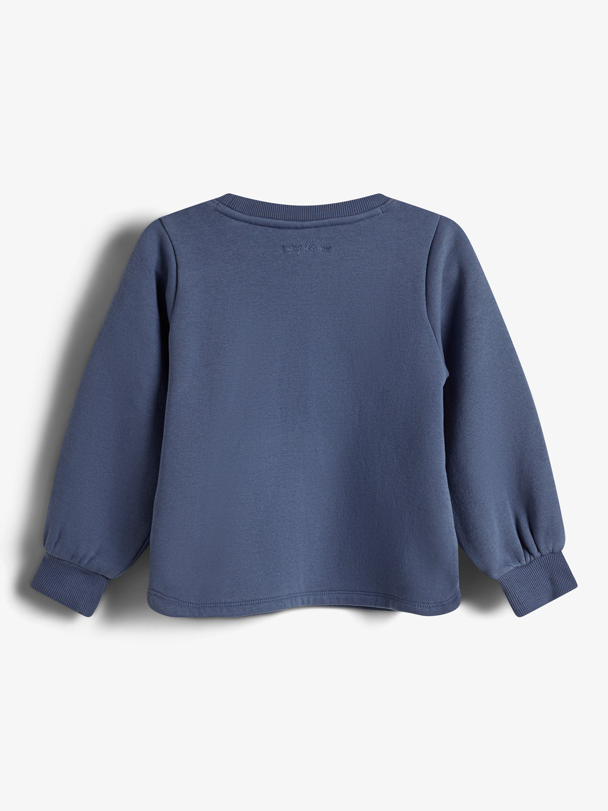 Ein hellblauer Pullover hängt leblos, zeigt die Rückseite mit gesticktem Text am oberen Rücken. Lange Ärmel mit Bündchen. Der Hintergrund ist weiß. Text: "name it is" (nur teilweise lesbar).