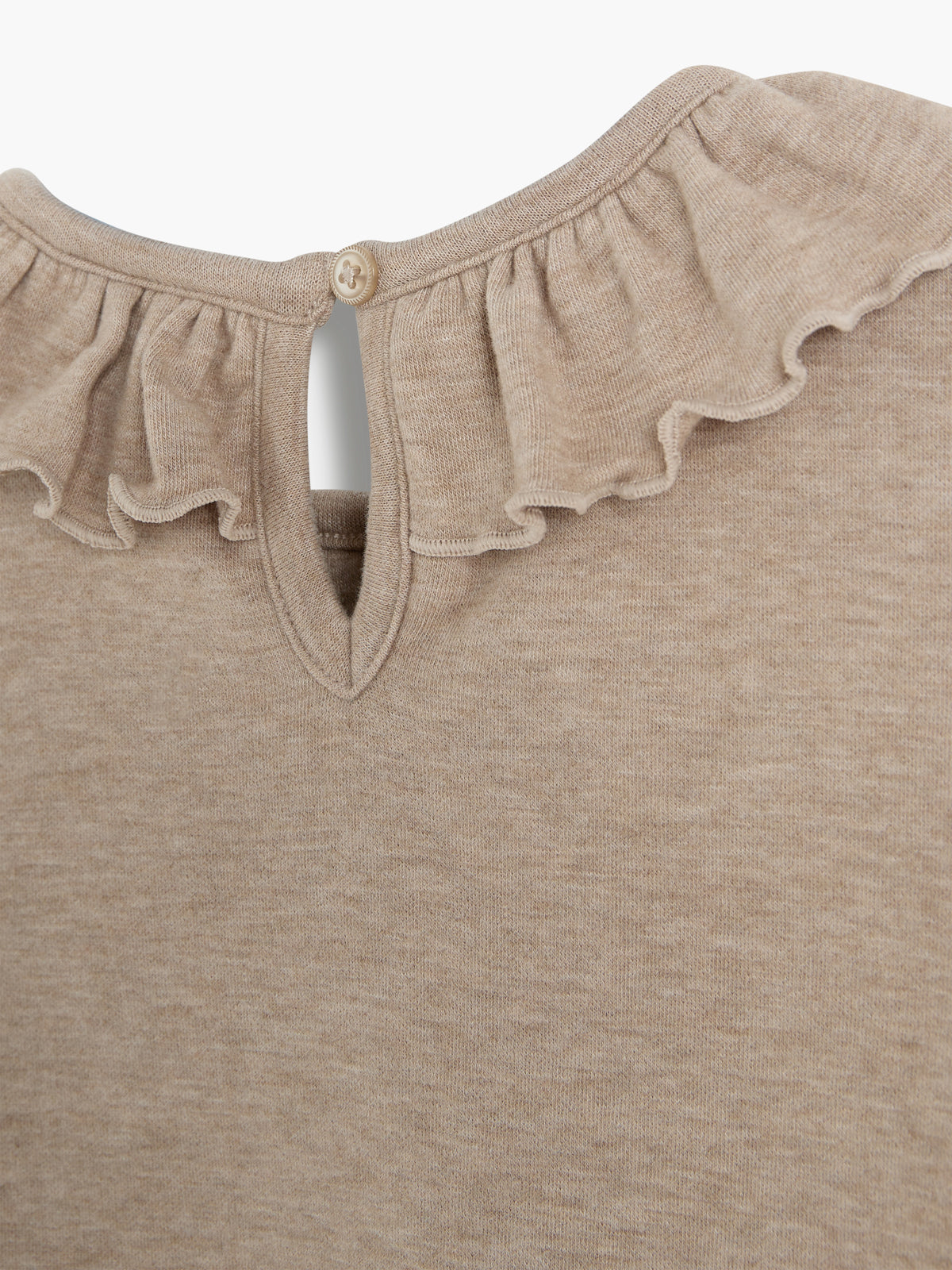 A beige garment with a ruffled neckline features a button closure and teardrop-shaped cutout at the back, displayed against a plain backdrop.