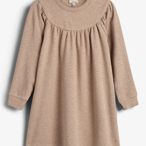 Ein beige Kinderkleid mit langen Ärmeln, Rundhalsausschnitt und gerafftem Brustbereich, hängt vor einem weißen Hintergrund. Im Nackenetikett steht "smile_love".