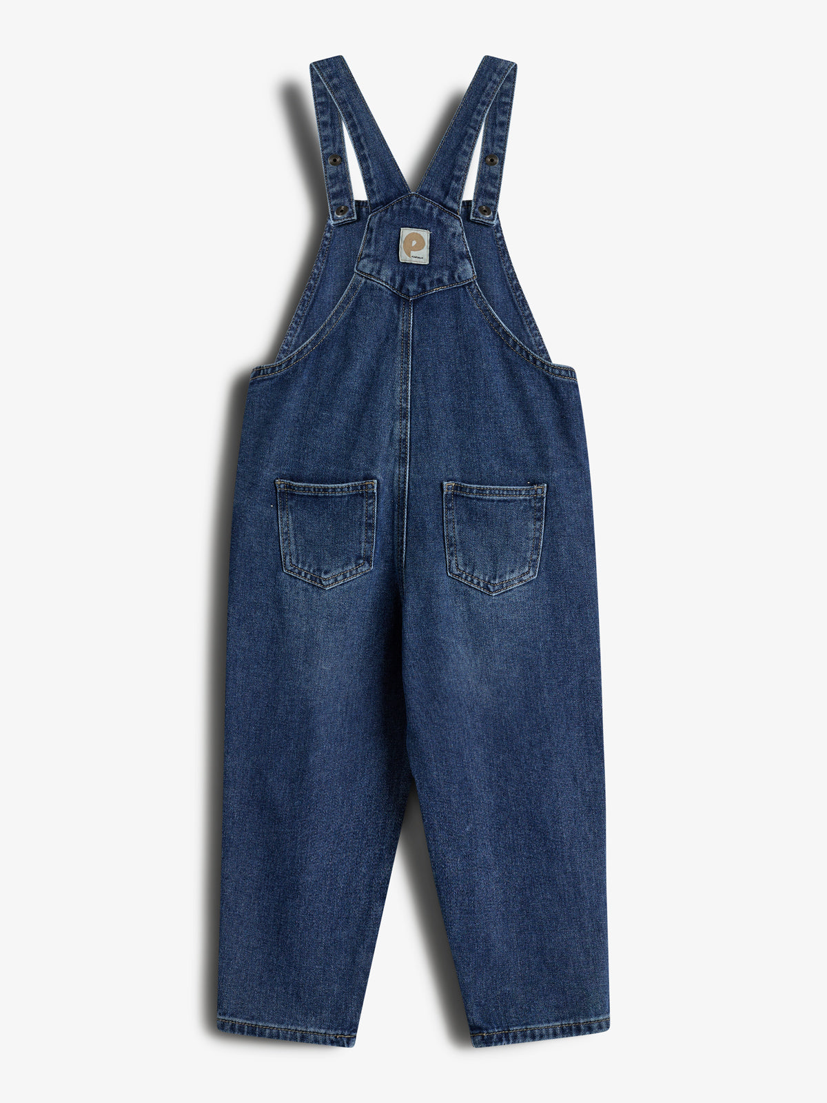 Eine blaue Jeans-Latzhose hängt vor einem weißen Hintergrund. Sie hat breite Träger, zwei vordere Taschen und ein kleines Logo-Etikett auf der Brust.