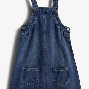 Jeanskleid mit Trägern und zwei Vordertaschen liegt flach auf weißem Hintergrund. Nieten an den Trägern verleihen dem Kleid Struktur. Kontextlos präsentiert, ohne sichtbare Umgebung.