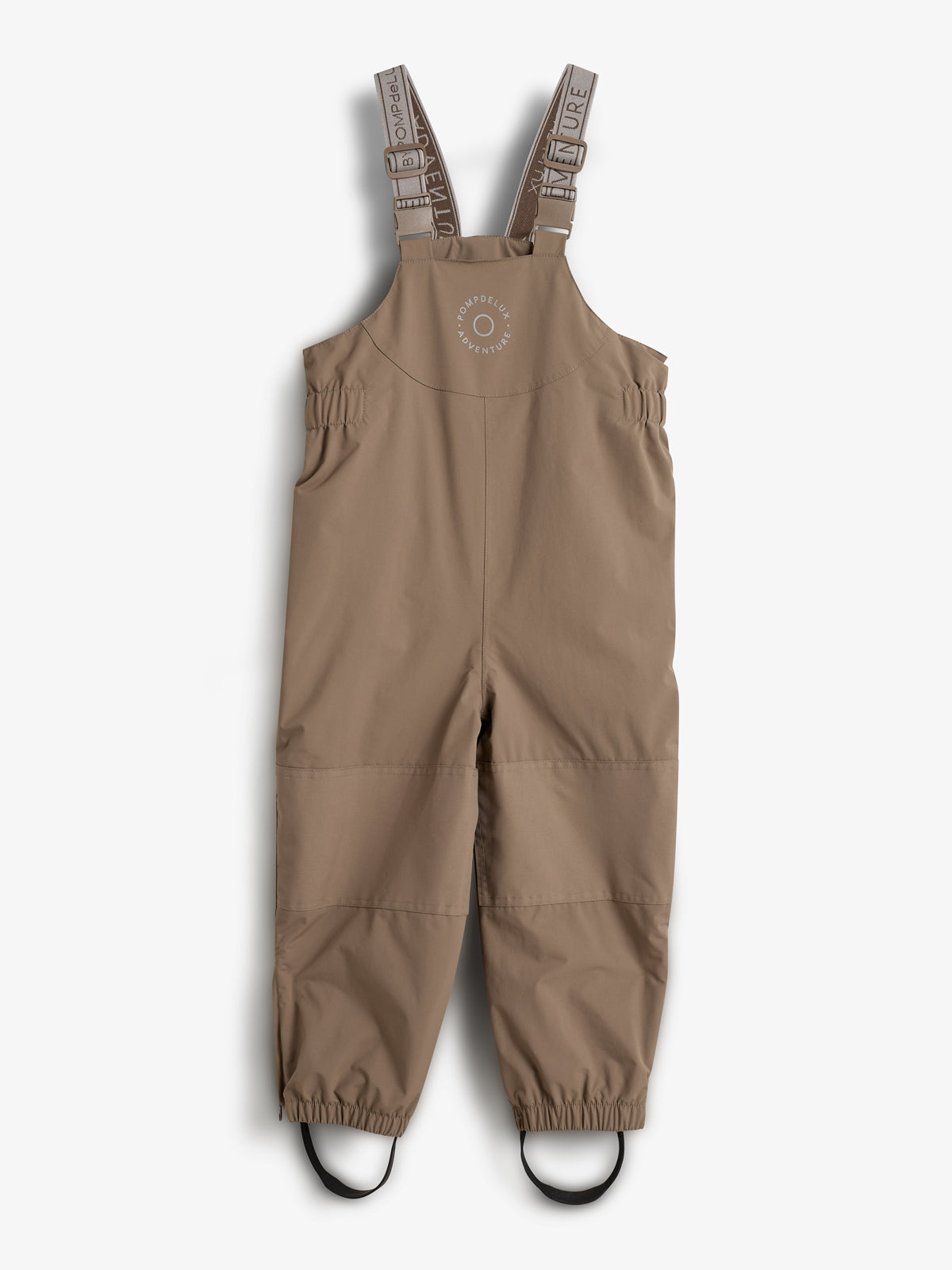 Eine beige Latzhose für Kinder hängt ruhig. Der Stoff hat elastische Beine mit Fußschlaufen. Auf der Latzhose steht: "OUTER ADVENTURE OMPDELUX". Sie hängt vor einem neutralen weißen Hintergrund.