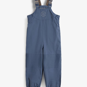 Ein blauer Kinder-Schneeoverall hängt gerade mit elastischen Trägern, die mit "ADVENTURE BY POMPDELUX" beschriftet sind, auf einer weißen Fläche. Text auf der Brust: "POMPDELUX ADVENTURE".