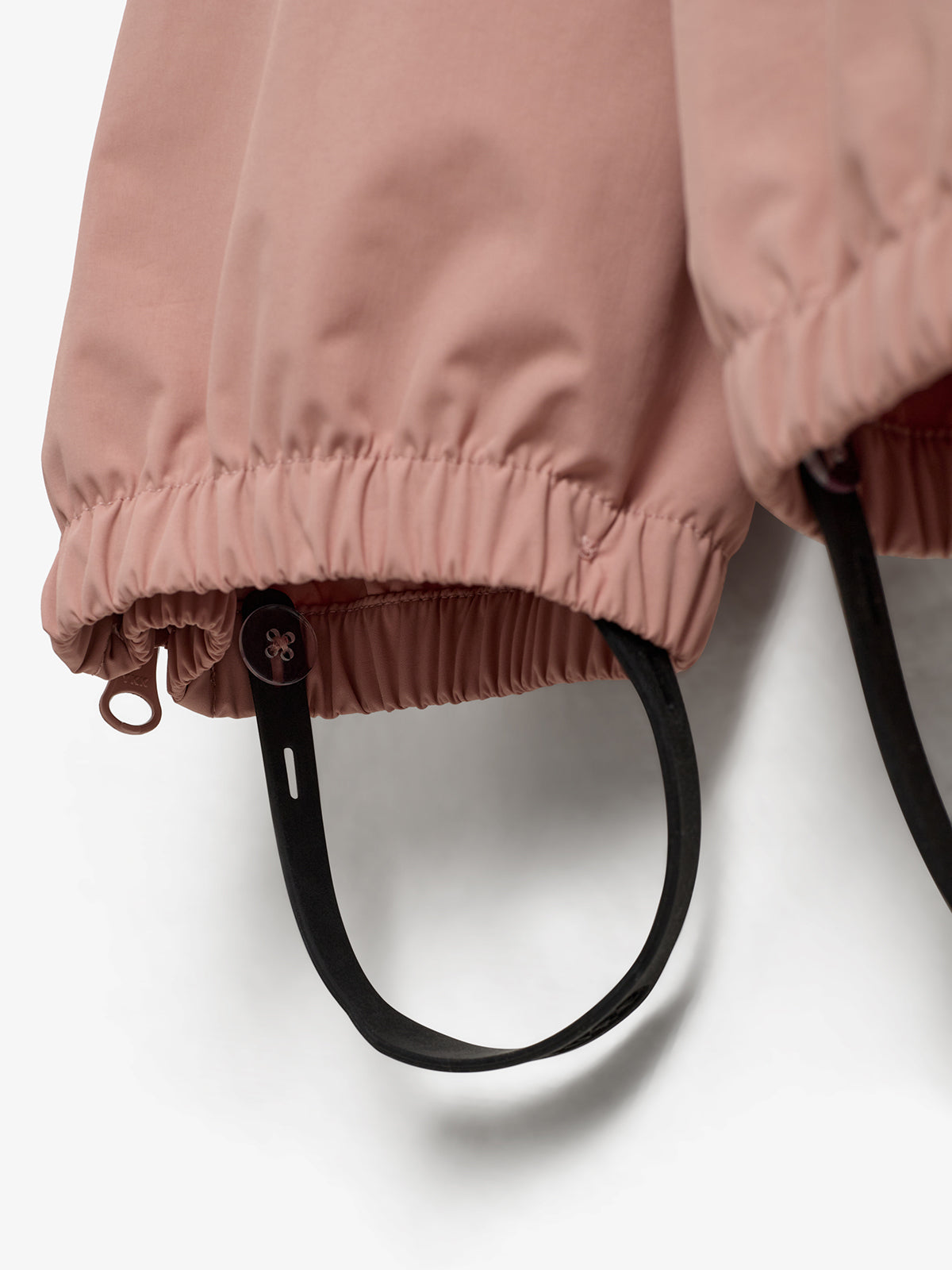 Rosa Ärmel mit elastischen Bündchen halten schwarze Riemen; drahtige Struktur und Ösen betonen Funktionalität. Helle, schlichte Umgebung bietet Kontrast.