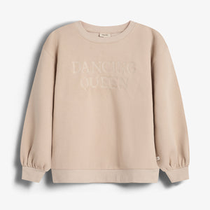 Ein beige Sweatshirt mit gerippten Bündchen und Rundhalsausschnitt zeigt den aufgedruckten Text "DANCING QUEEN". Es hängt vor einem weißen Hintergrund.