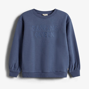 Blauer Pullover mit der gestickten Aufschrift "DANCING QUEEN" auf der Vorderseite, hängt vor einem neutralen, hellen Hintergrund.