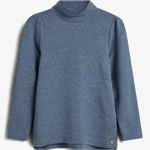 A blue long-sleeve turtleneck shirt hangs against a white background, featuring clean lines and a small, gold heart emblem near the hem.