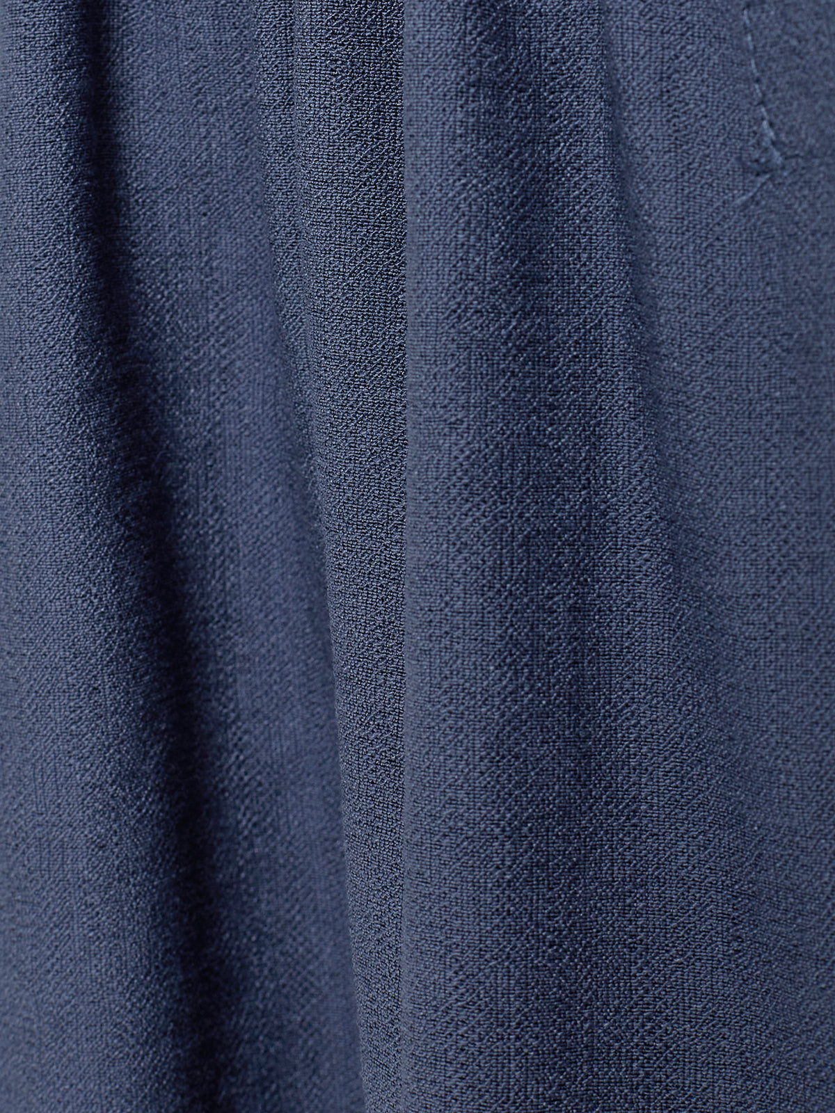 Ein blauer Stoffvorhang hängt ruhig. Die Textur ist grob und die Oberfläche weist leichte Wellen auf. Die Umgebung ist nicht sichtbar.