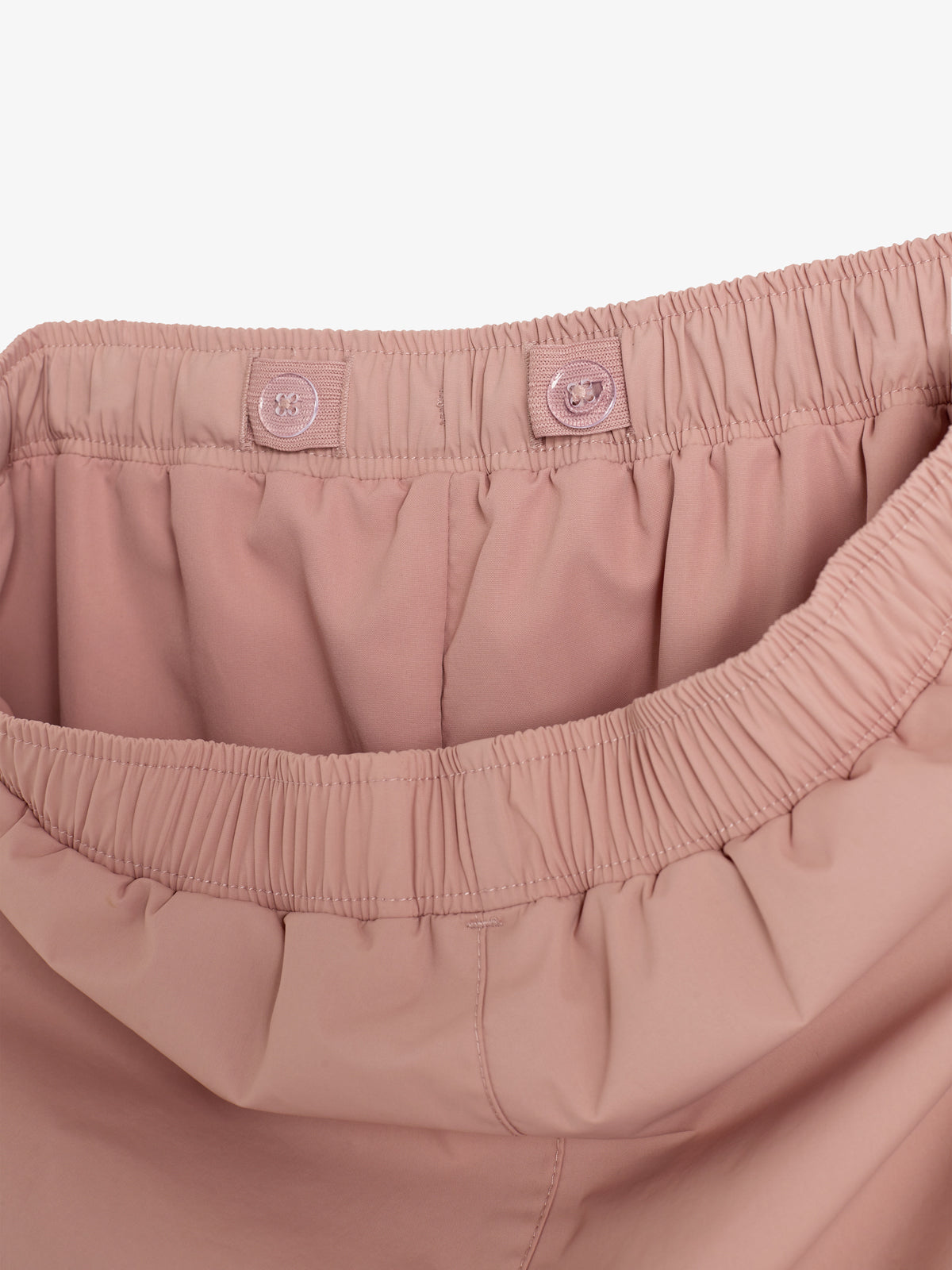 Rosa Hose mit elastischem Bund zeigt Knopflöcher für Anpassung. Hintergrund ist neutral und fokussiert auf Hosenbunddetails.